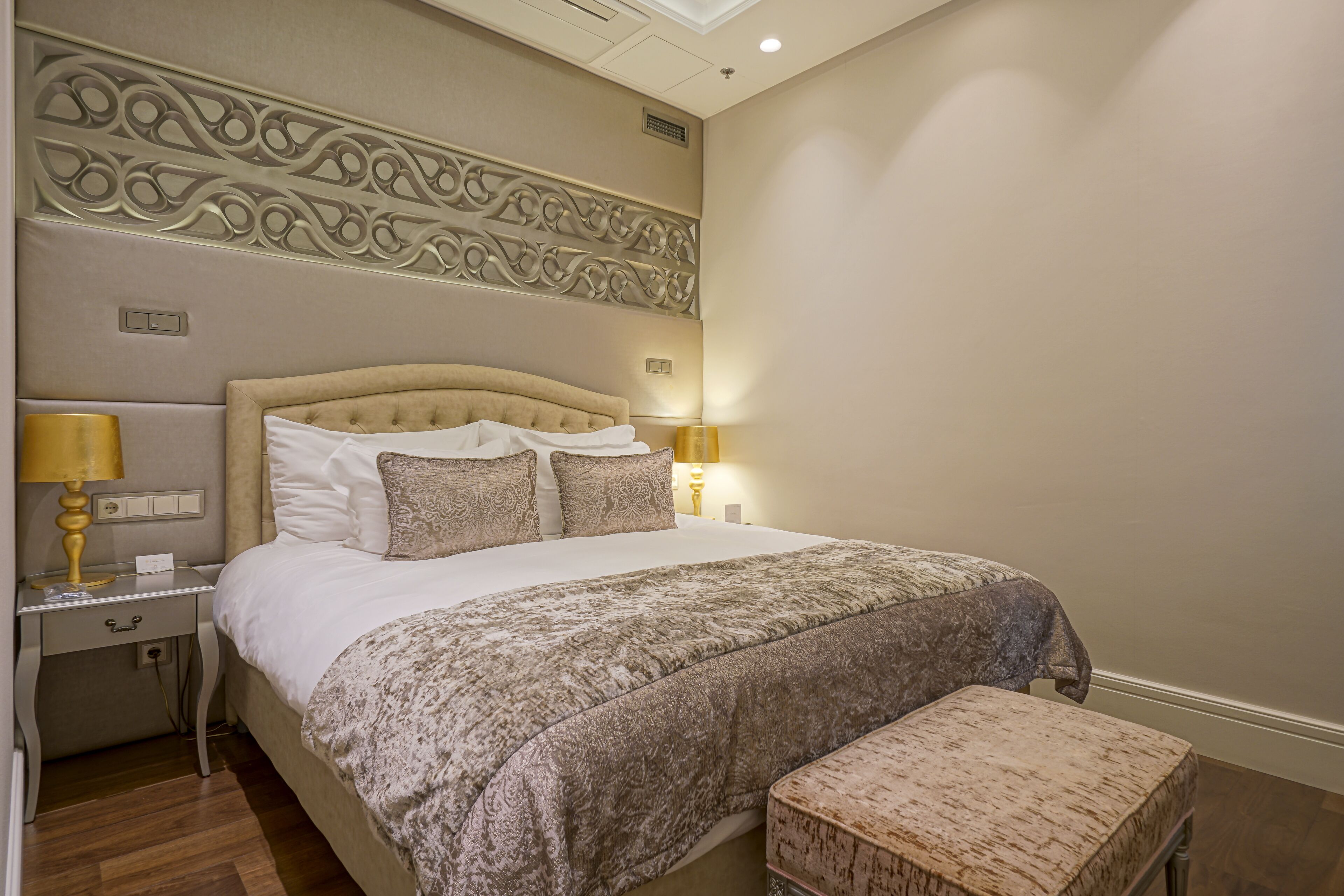 Un dormitorio ordenado con una cama grande, lámparas de noche y un cabecero decorativo.