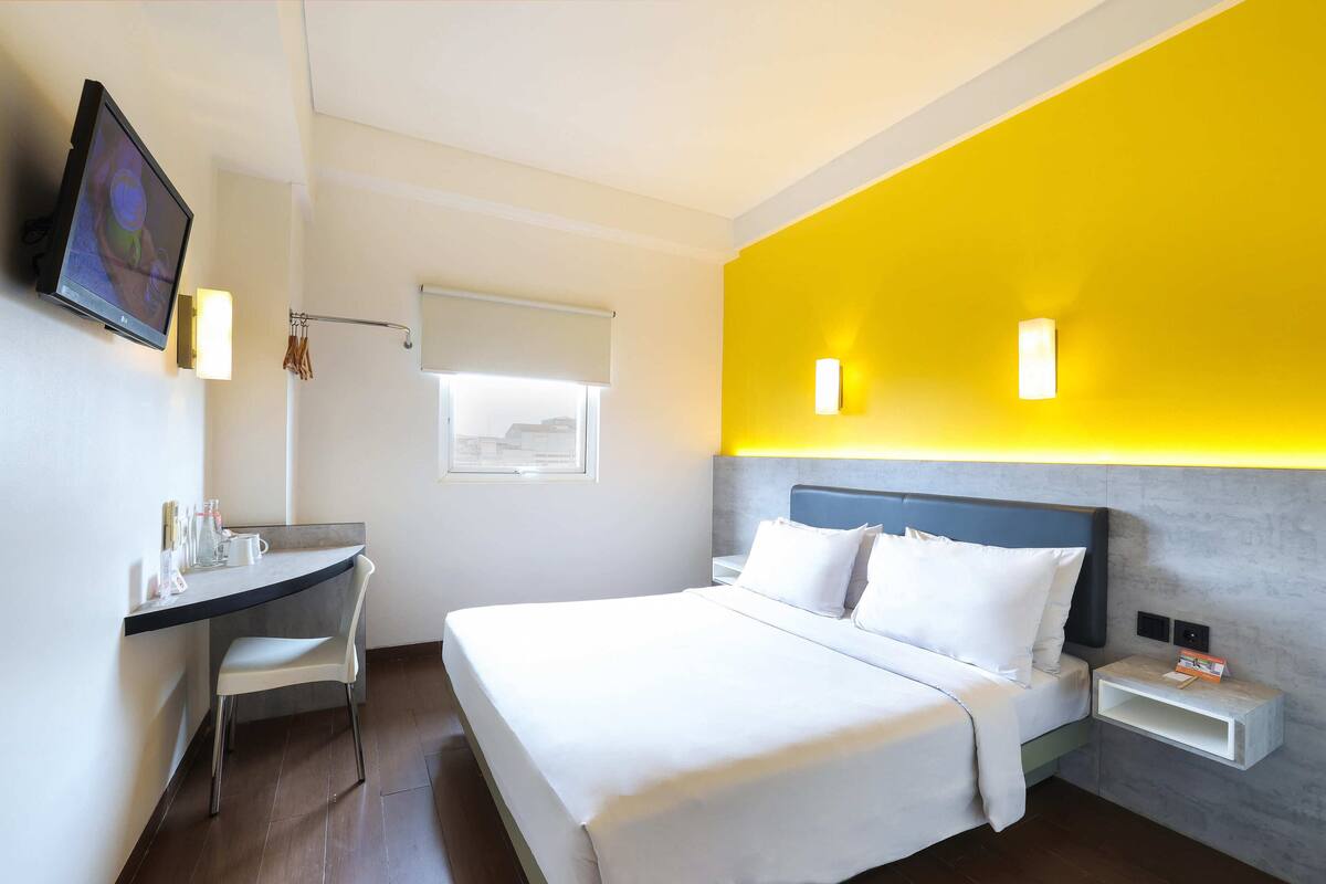 Une chambre d’hôtel équipée d’un lit, d’un bureau, d’une chaise, d’une télévision et d’une fenêtre avec un store.