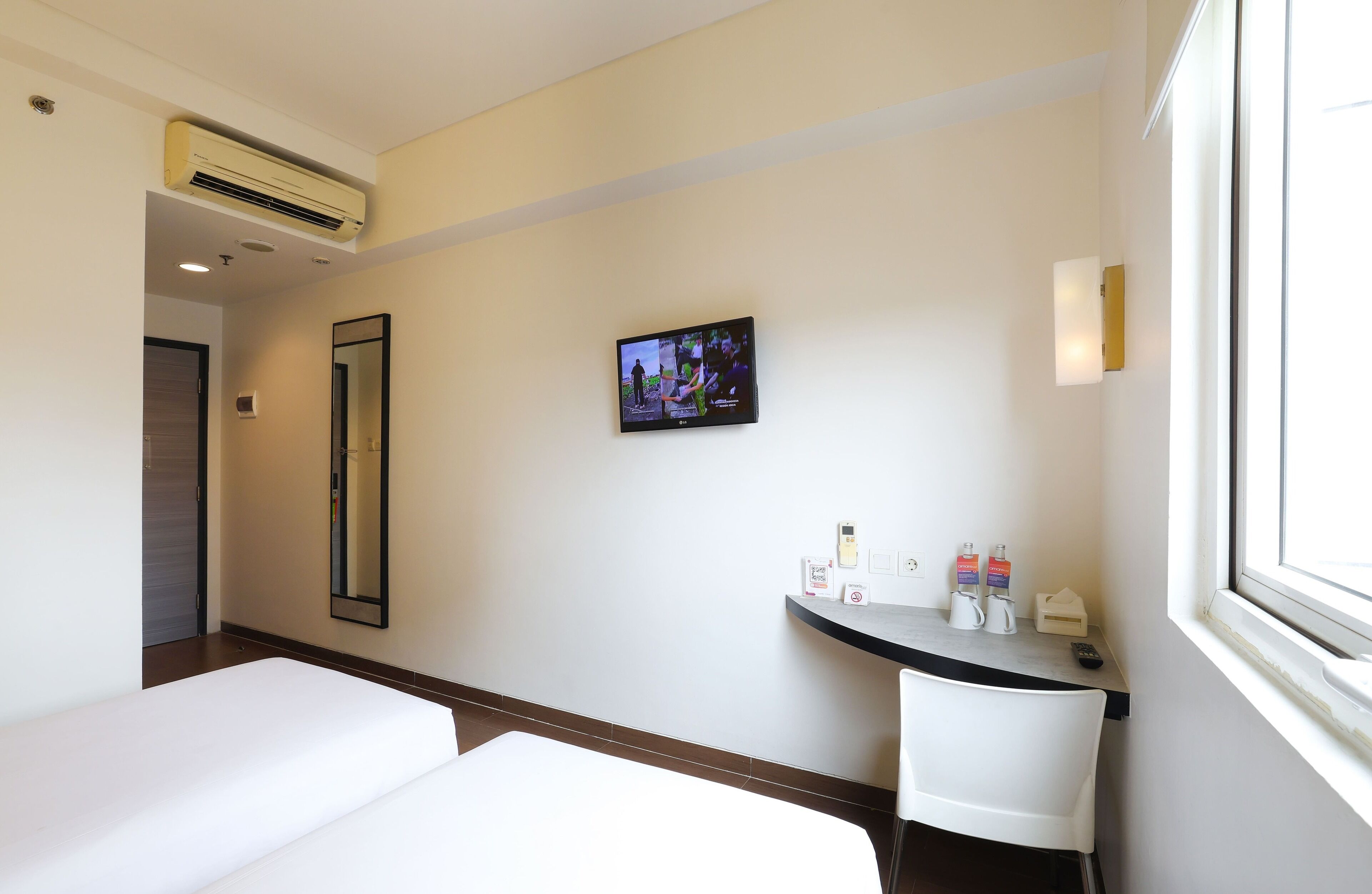 Ein Hotelzimmer mit einem Bett, einem Schreibtisch mit Toiletteurzeugnissen, einem Fernseher und einem Fenster.