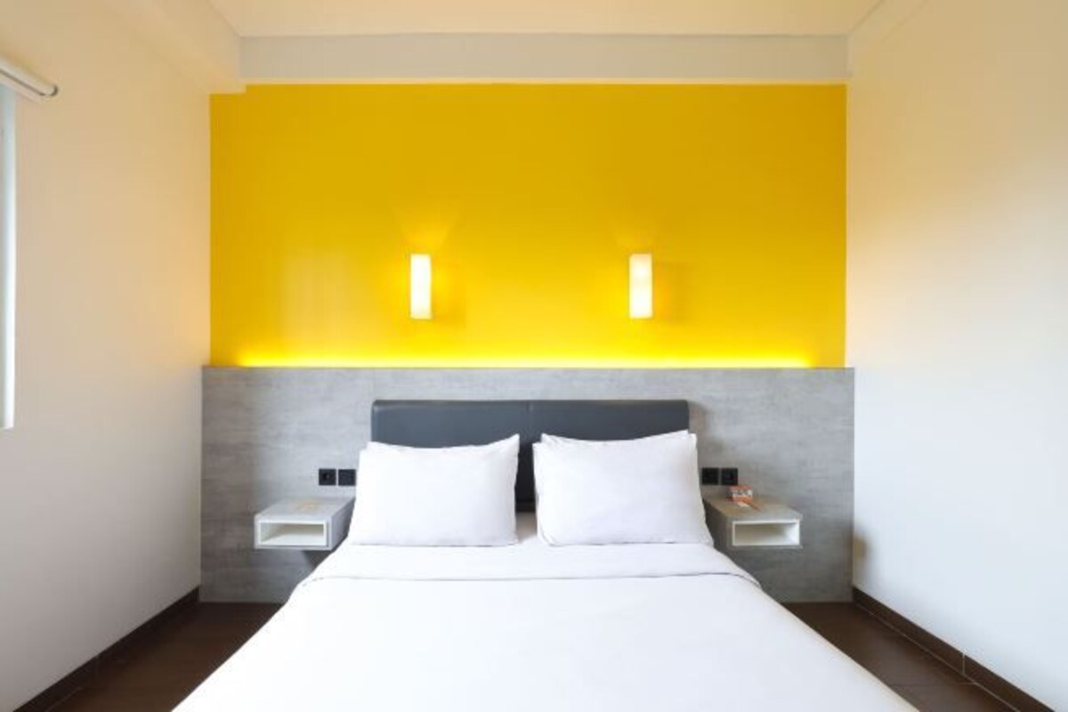 Una habitación de hotel moderna con una cama, dos mesitas de noche y una pared de color amarillo brillante.