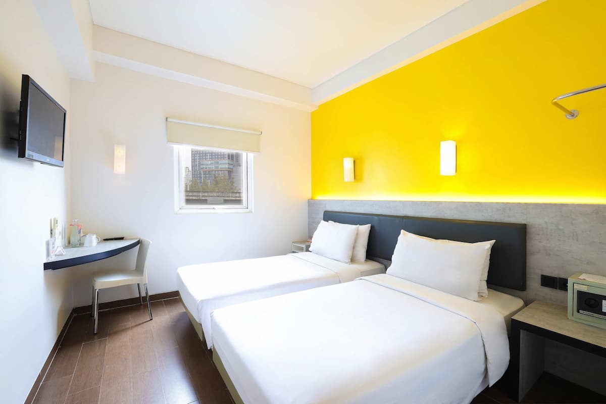 Une chambre d’hôtel avec deux lits, un bureau, une télévision, une fenêtre et un mur d’accent d’un jaune vif.