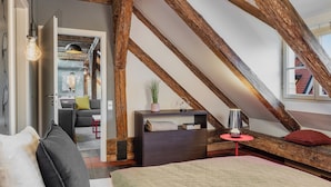 A bedroom with exposed wooden beams, a bed, a bedside table, a lamp, and a window with a view of a red-roofed building. - 4 Arts Apartments by Adrez Living (Prague)