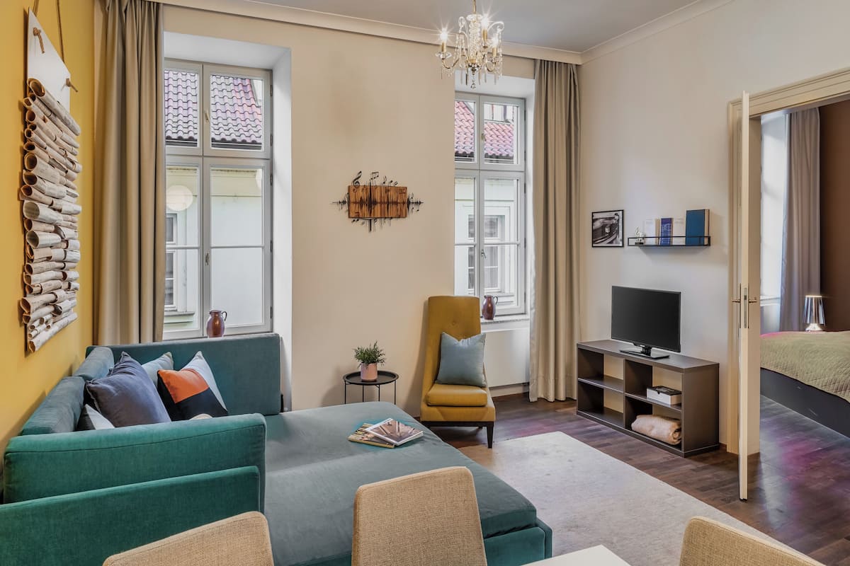 Un salon moderne avec un canapé turquoise, une petite table ronde ornée d’une plante, un fauteuil jaune, un meuble pour la télévision et un lustre.