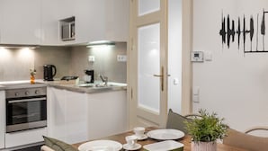 A modern kitchen with white cabinets, a microwave, and a coffee maker. There is a dining table with plates, cups, and a plant. - 4 Arts Apartments by Adrez Living (Prague)