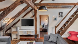 A loft-style living room with exposed wooden beams, a flat-screen TV, a red accent chair, and a staircase leading to an upper level. - 4 Arts Apartments by Adrez Living (Prague)