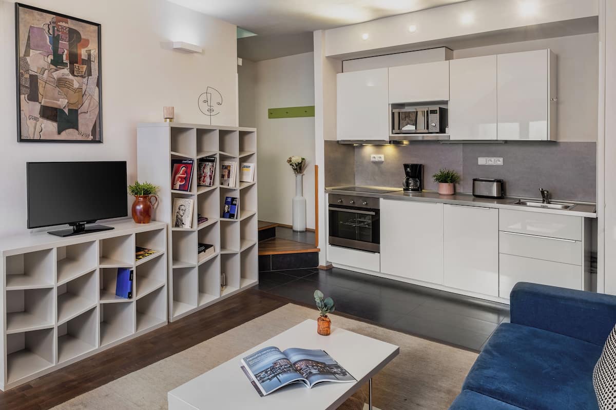Un salon moderne avec un téléviseur à écran plat, une bibliothèque, une table basse avec des magazines et un canapé bleu.