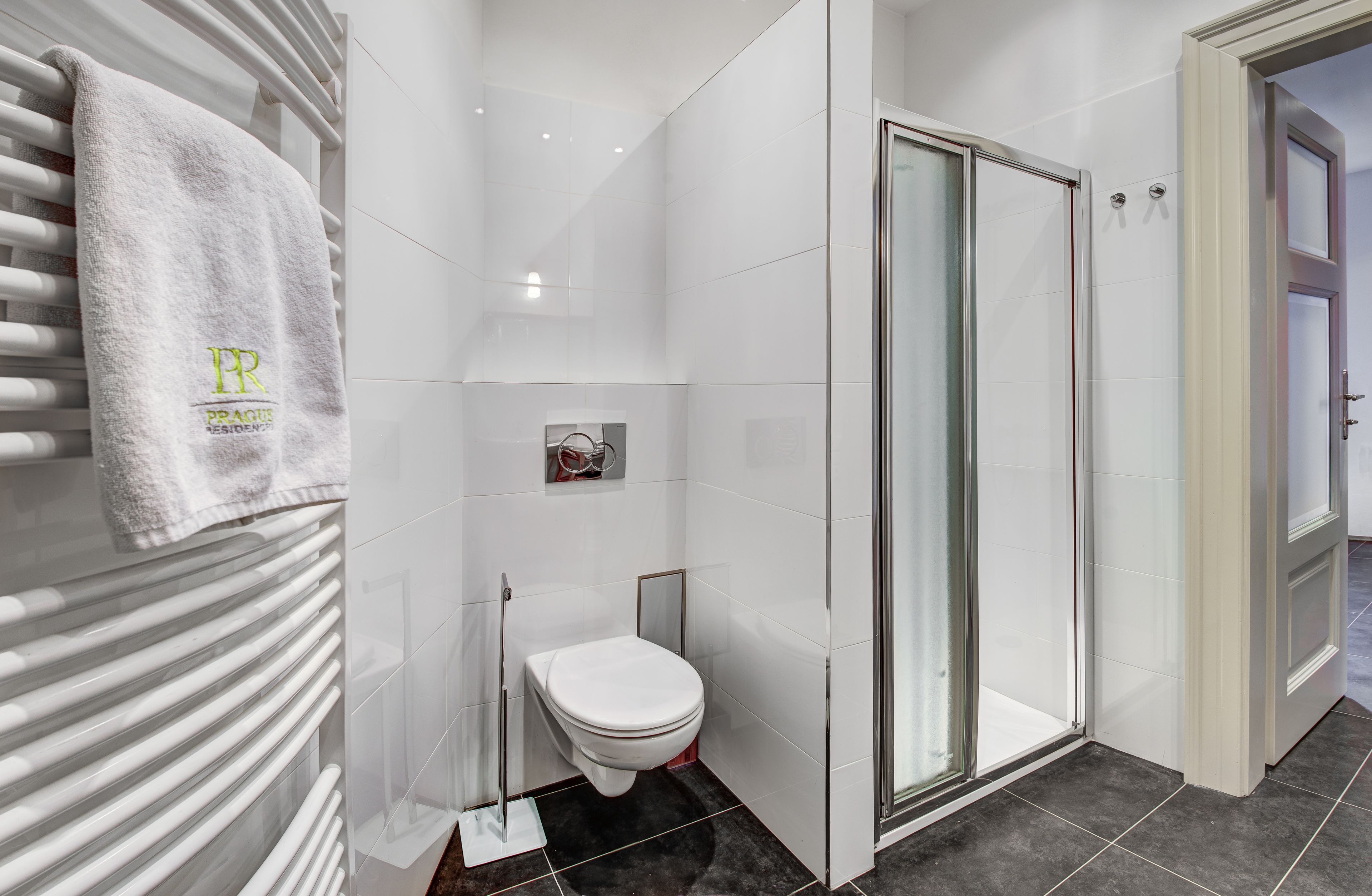 A modern bathroom with a white tiled shower, a toilet, and a towel rack with a logo.