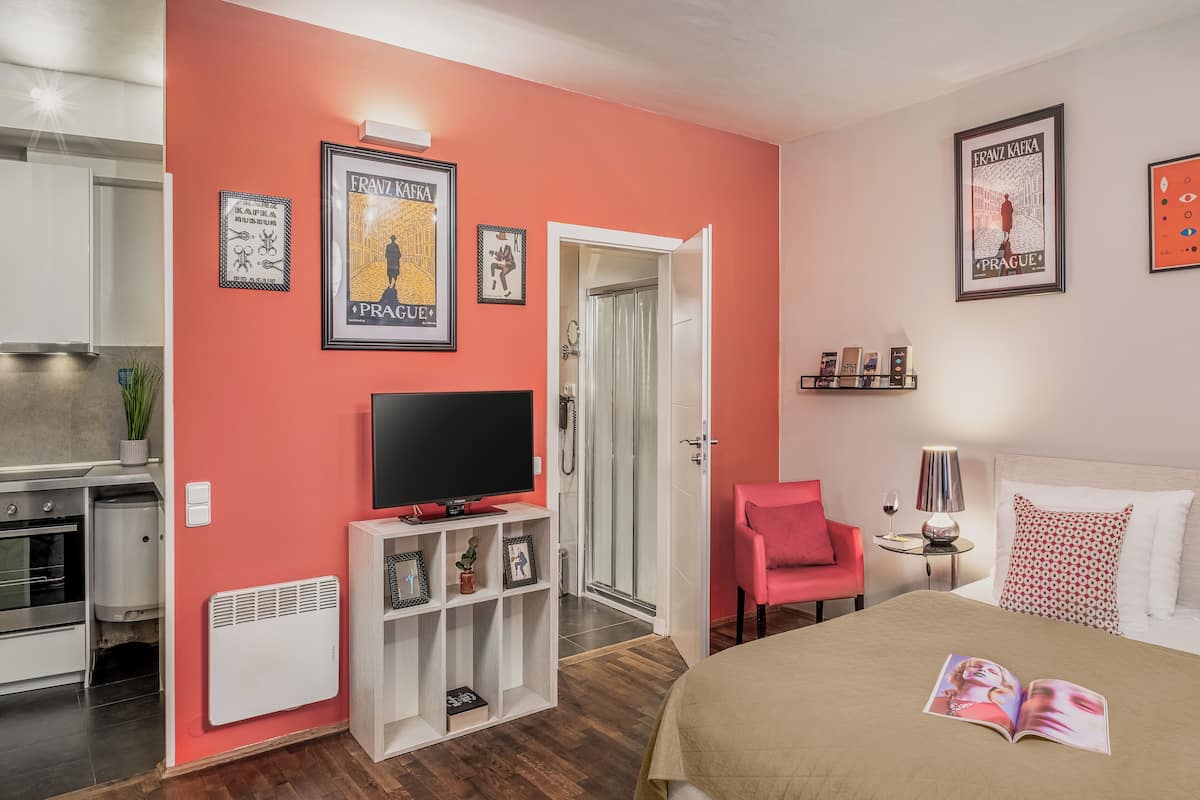 Une chambre moderne avec un lit, une télévision, un fauteuil rose et une bibliothèque.