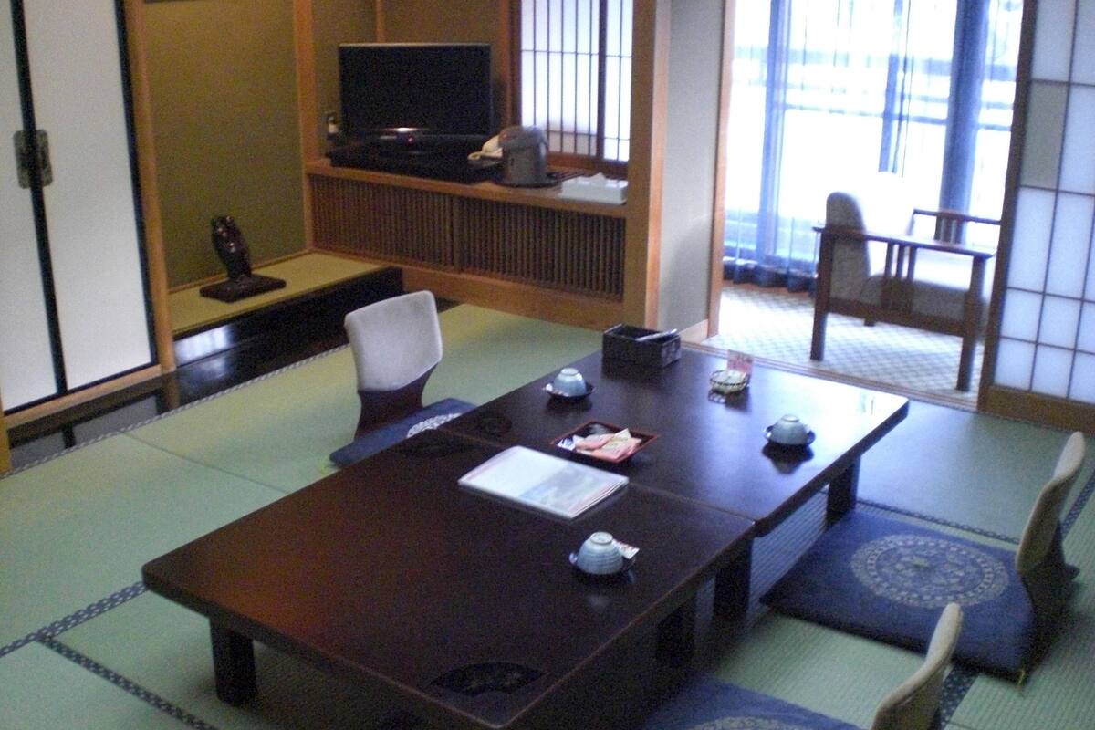A traditional Japanese meeting room with tatami flooring, a low table, and a television on a stand.