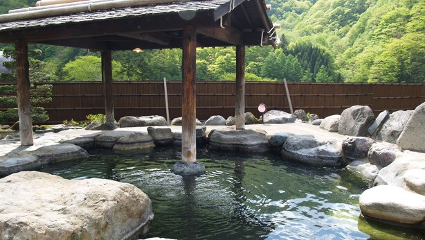 A traditional Japanese onsen with a wooden pavilion and large rocks surrounding a small pool of water. - Okada Ryokan Warakutei (Takayama)