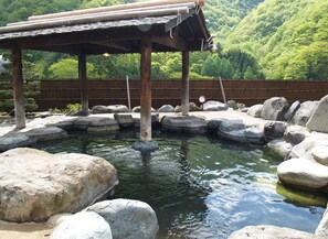 A traditional Japanese onsen with a wooden pavilion and large rocks surrounding a small pool of water. - Okada Ryokan Warakutei (Takayama)