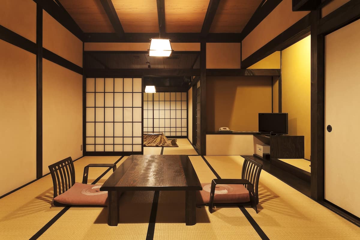A traditional Japanese room with tatami flooring, a low wooden table, and black chairs.