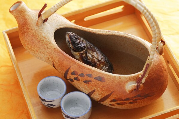 A ceramic fish in a decorative bowl with two small cups beside it. - Okada Ryokan Warakutei (Takayama)