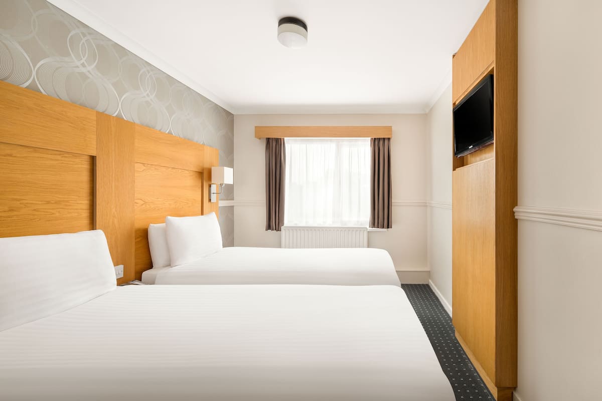 A hotel room with two beds, a wooden headboard, a flat-screen TV, and a window with curtains.