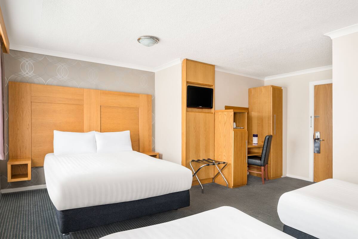 A hotel room with a large bed, a desk with a chair, a TV, and a wardrobe.