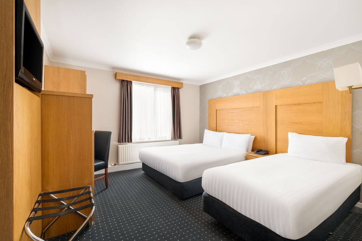 A hotel room with two beds, a desk, a chair, a TV, and a window with curtains.