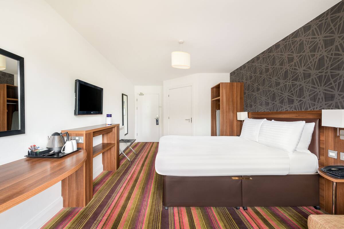 A hotel room with a bed, a desk, a television, and a patterned carpet.