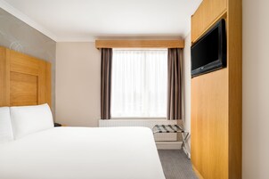 Een hotelkamer met een bed, een aan de muur bevestigde televisie, een raam met gordijnen en een radiator.