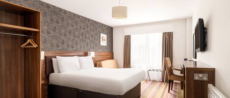 A hotel room with a bed, a desk, a chair, a TV, and a wardrobe.