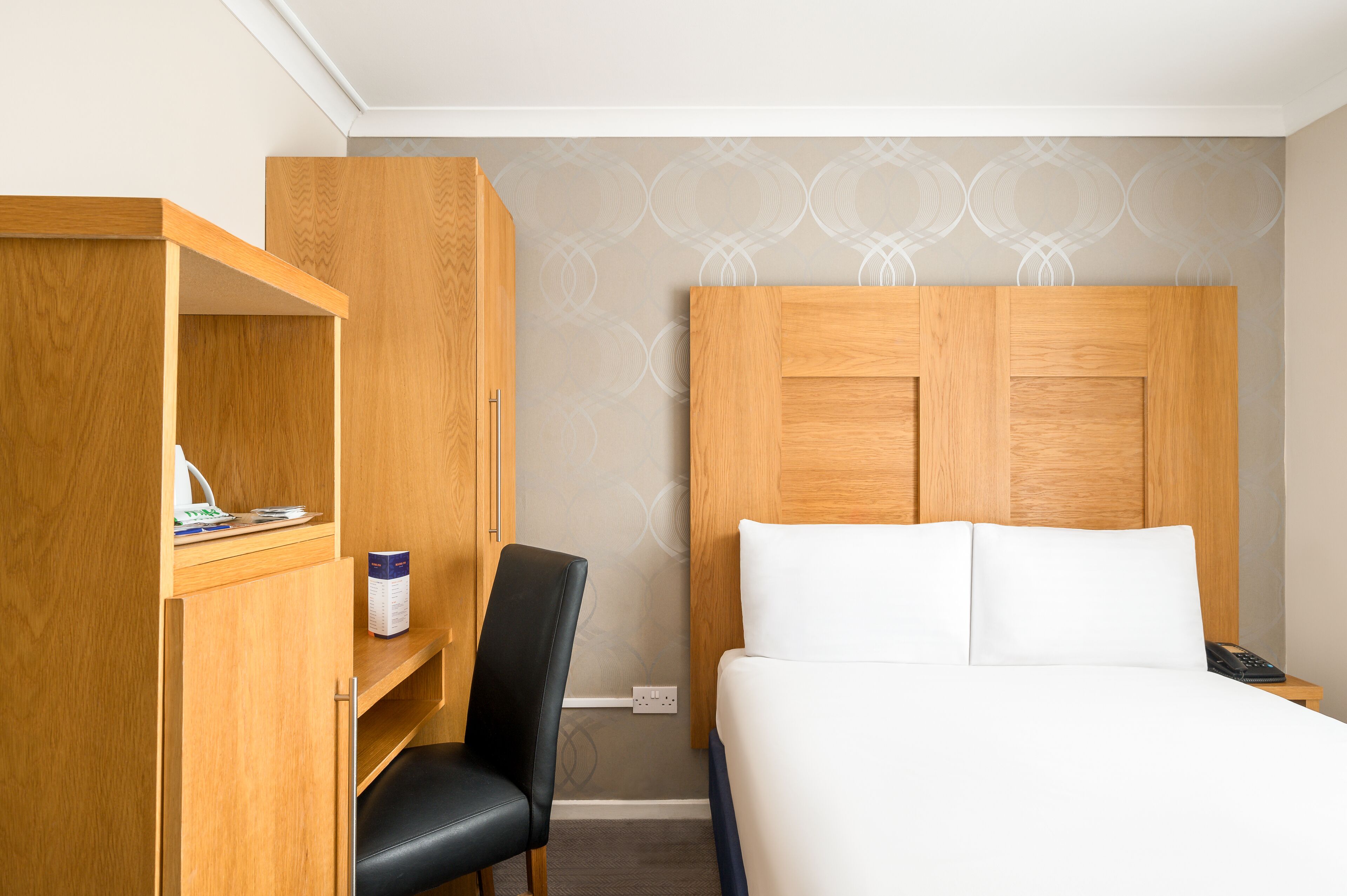 Een hotelkamer met een bed, een houten garderobe, een bureau en een stoel.