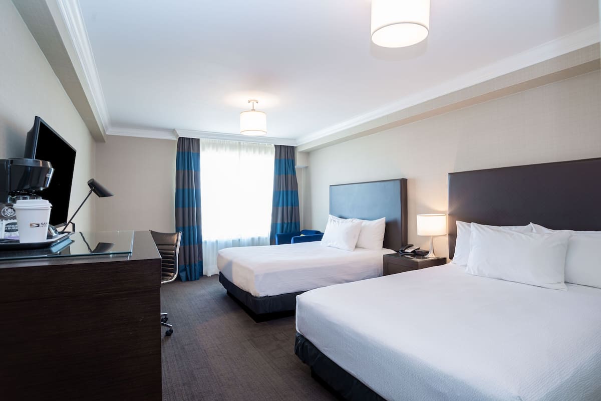 A hotel room with two beds, a desk with a coffee maker, a TV, and a lamp.