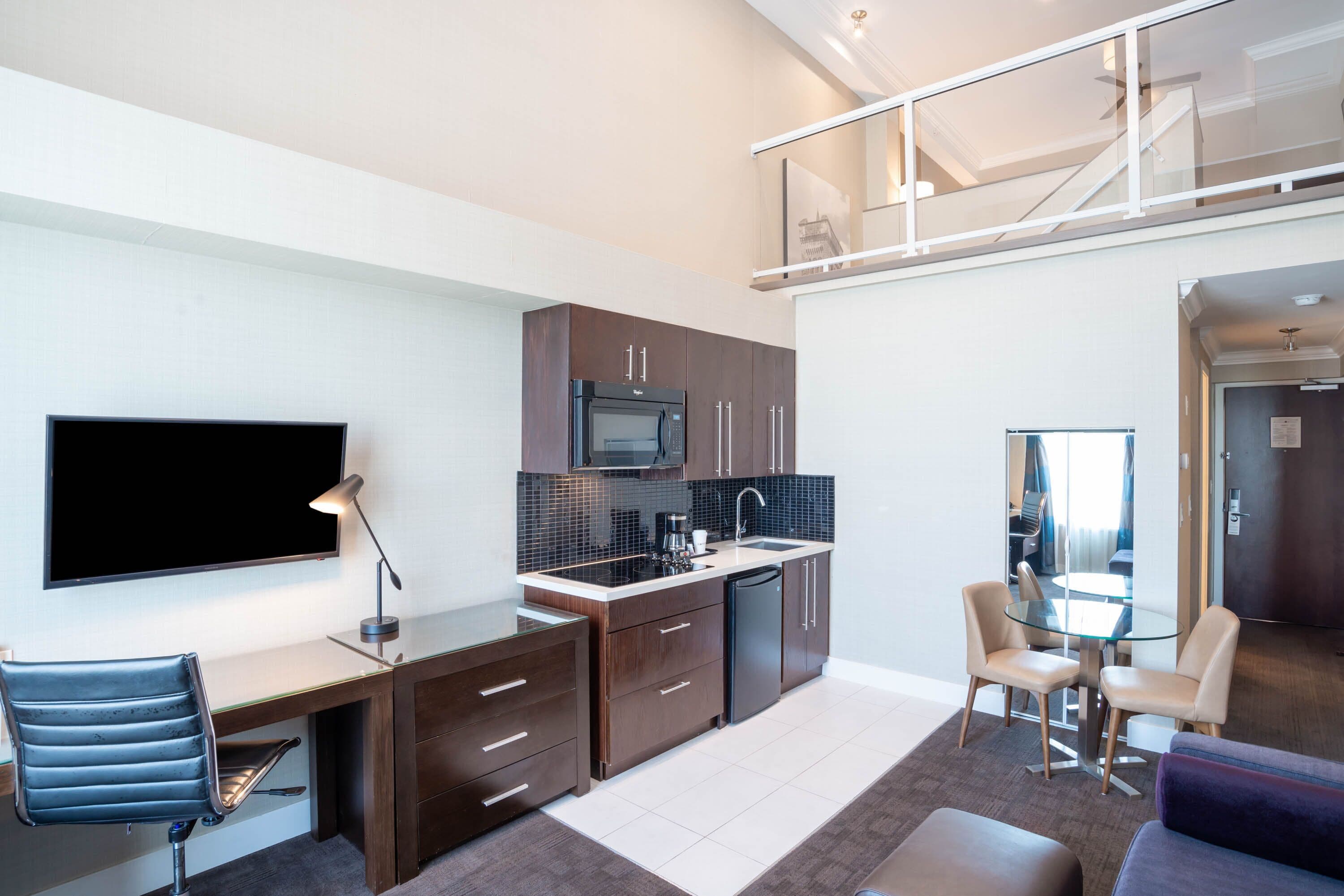 A modern kitchen with a flat-screen TV, a dining area with a glass table, and a sofa.
