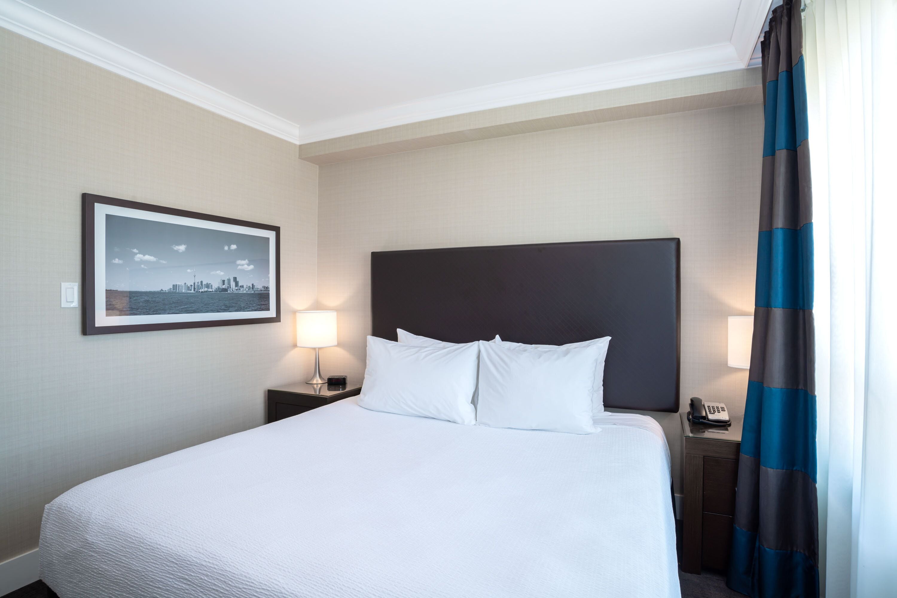 Habitación de hotel con una cama grande, una mesita de noche con lámpara, un cuadro en la pared y un teléfono.