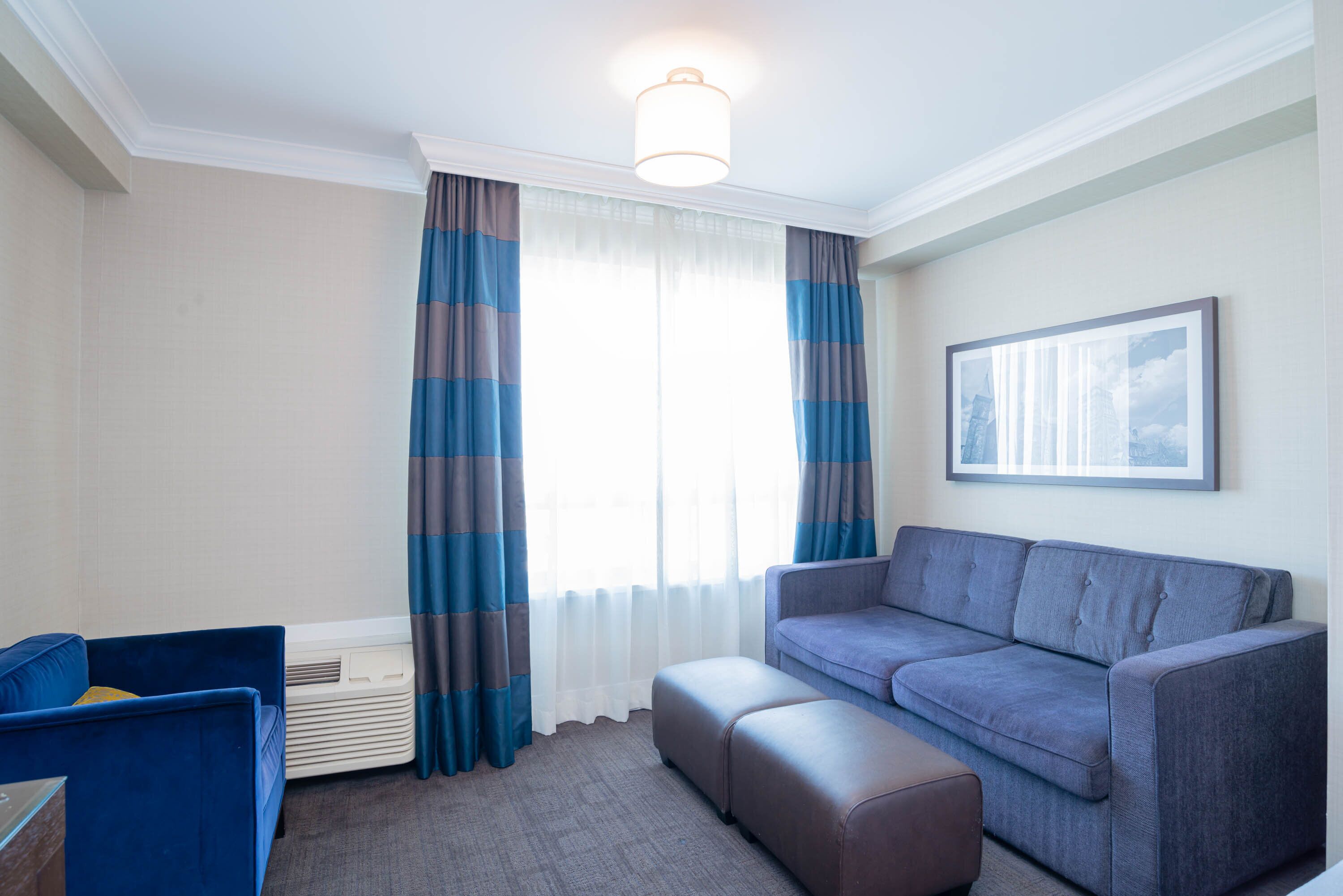 A modern living room with a grey sofa, a blue armchair, and a large window with striped curtains.