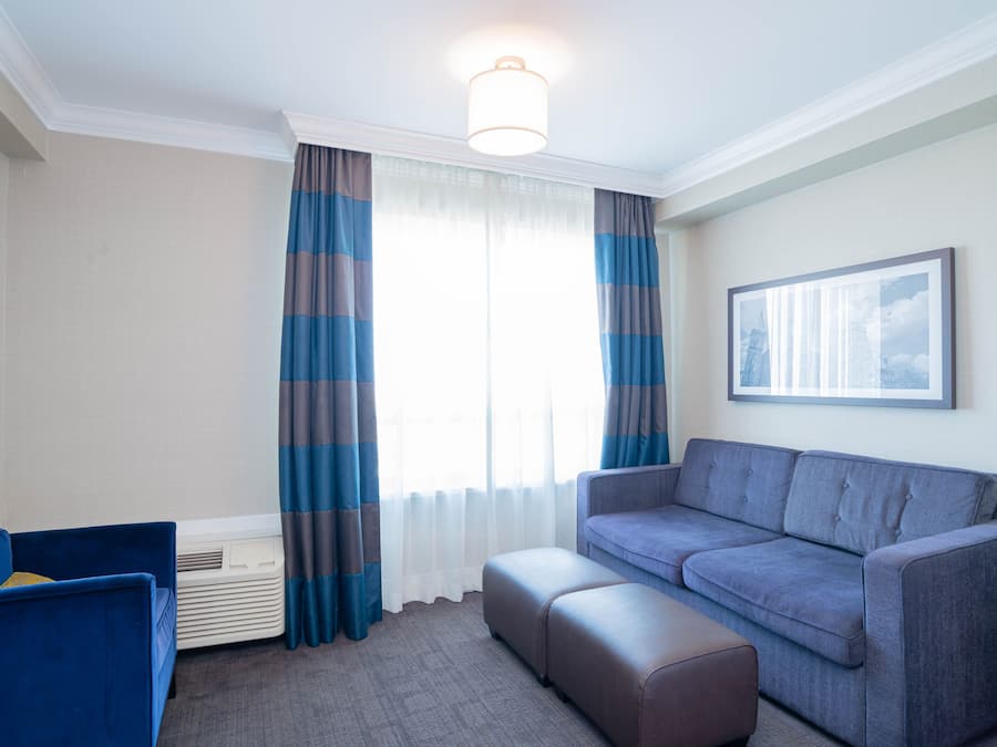 A modern living room with a grey sofa, a blue armchair, and a large window with striped curtains.