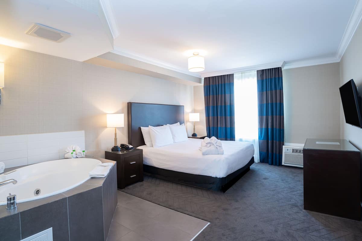 A hotel room with a large bed, a separate bathroom with a bathtub, a desk, and a flat-screen TV.