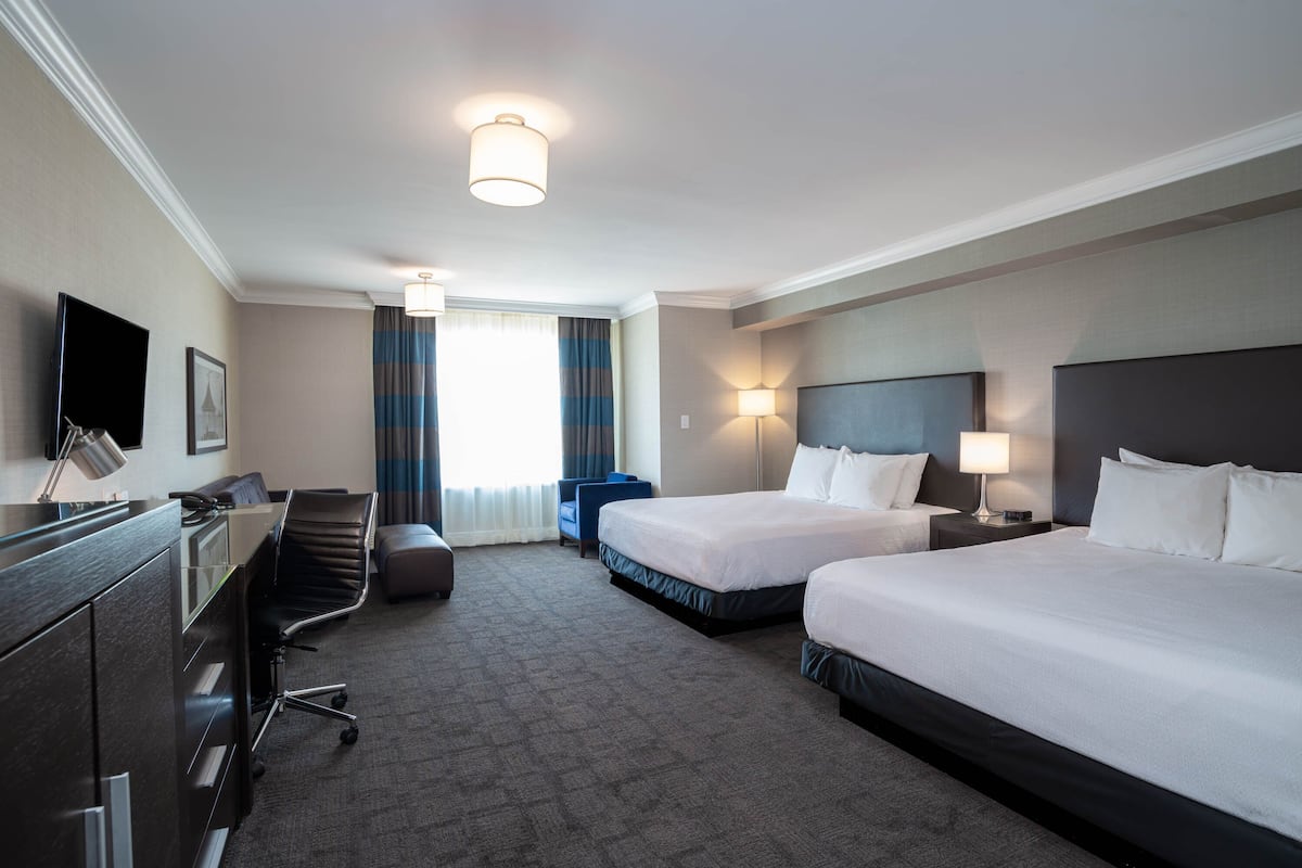 A hotel room with two beds, a desk, a chair, a TV, and a window with curtains.