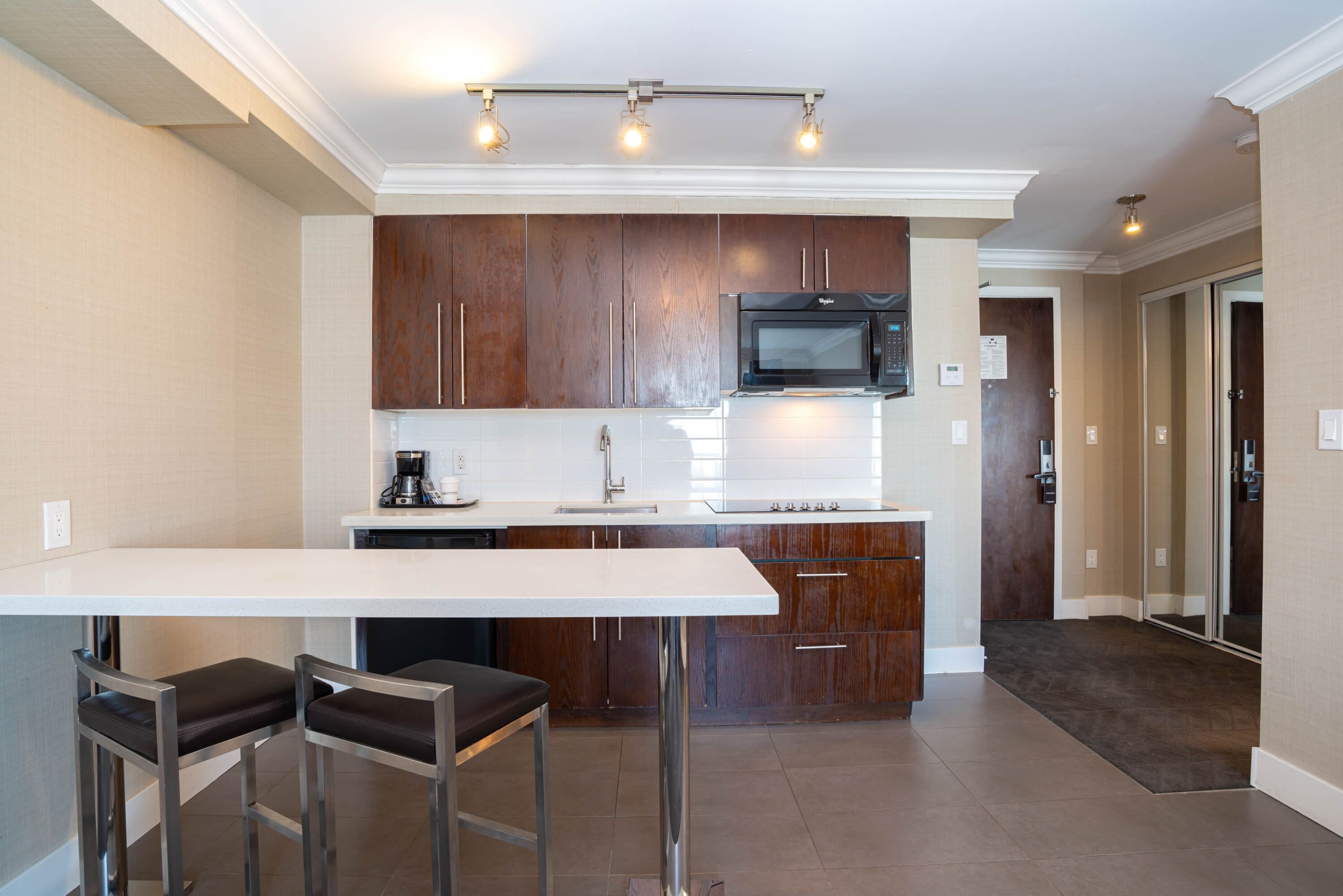 A modern kitchen with a white countertop, stainless steel bar stools, and wooden cabinets.