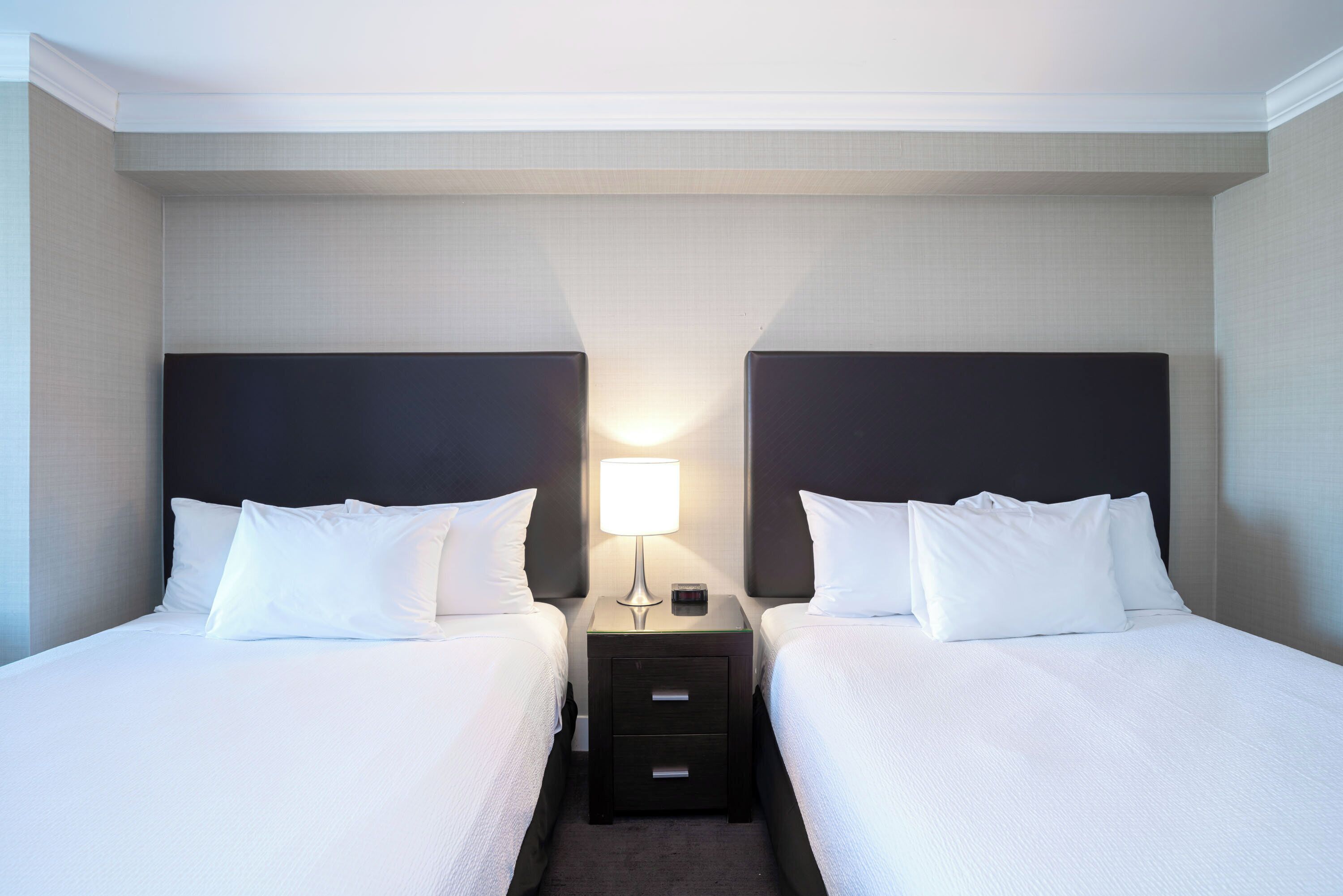 Habitació d'hotel amb dos llits individuals, una tauleta de nit amb una làmpada i un calaix petit.