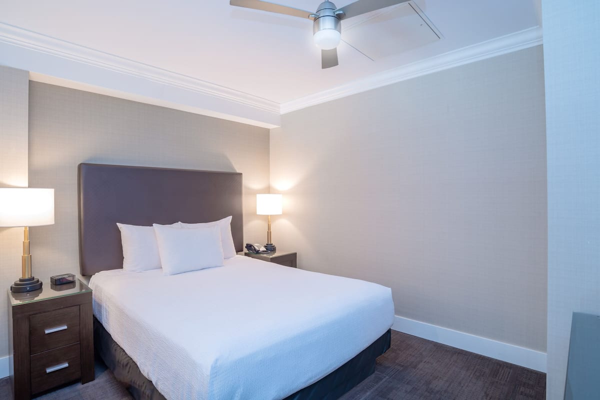 A neatly made bed with white linens, a dark headboard, and two bedside lamps.