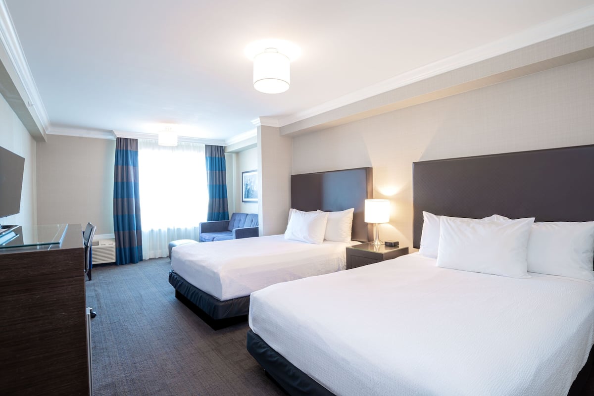 A hotel room with two beds, a desk, and a TV.