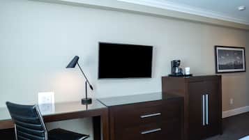 A hotel room with a desk, a chair, a television, a coffee maker, and a framed picture on the wall.