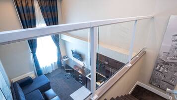 A modern apartment with a glass railing, a sofa, a desk, and a staircase.