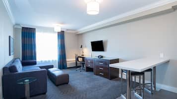 Una habitación de hotel con sofá, escritorio, silla, televisor y una mesita.