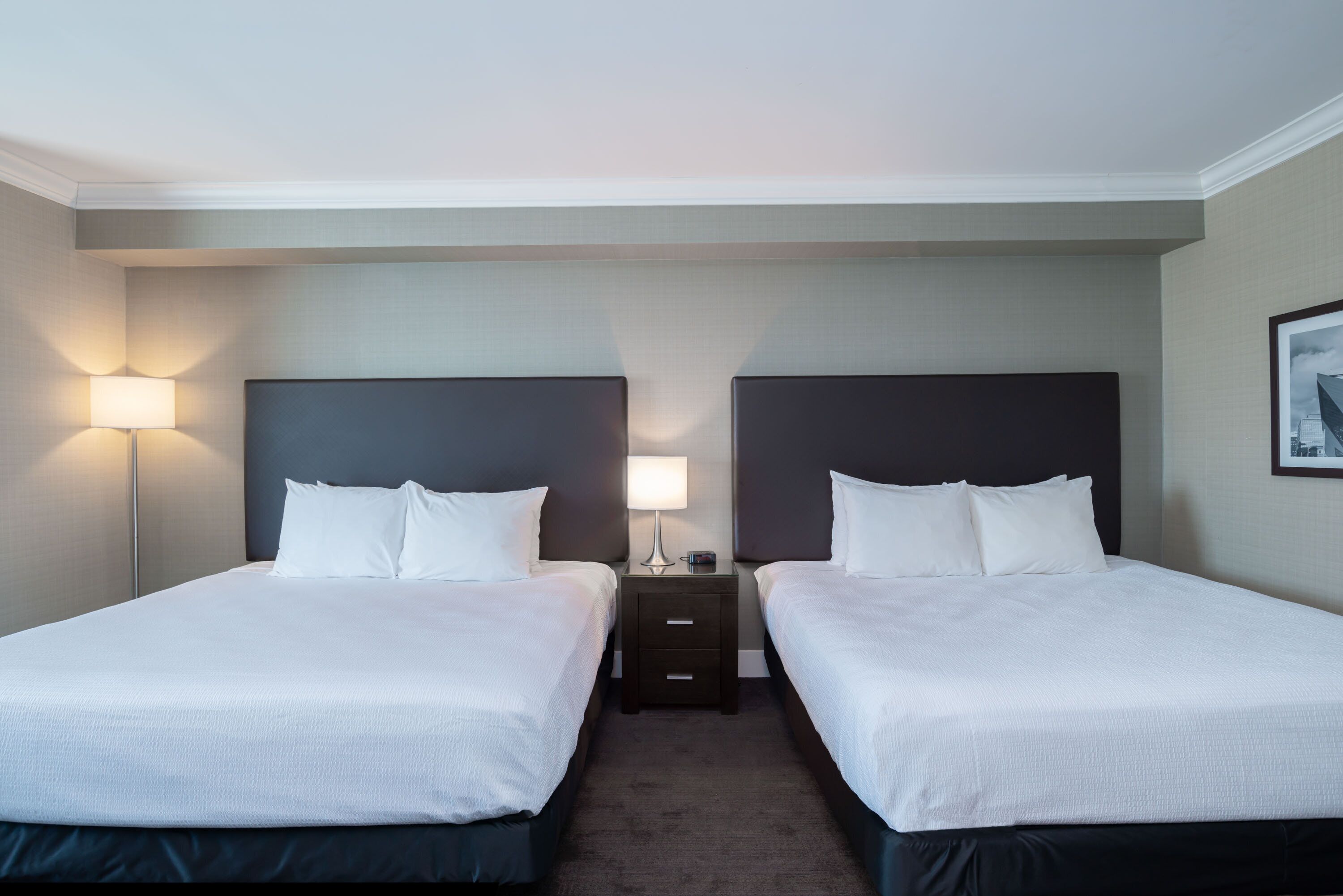 A hotel room with two beds, a nightstand with a lamp, and a framed picture on the wall.