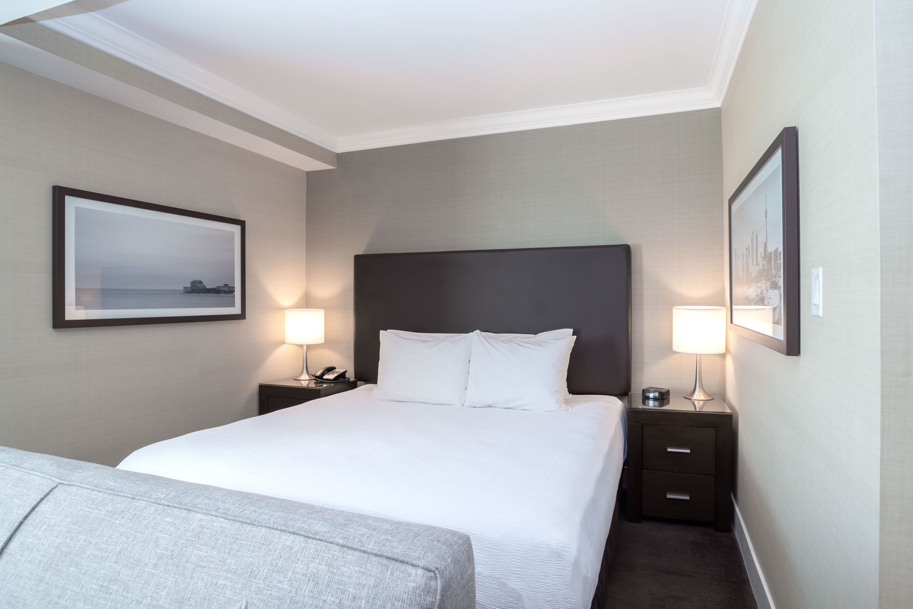 Une chambre d’hôtel avec un grand lit, deux tables de chevet avec des lampes et des tableaux encadrés aux murs.