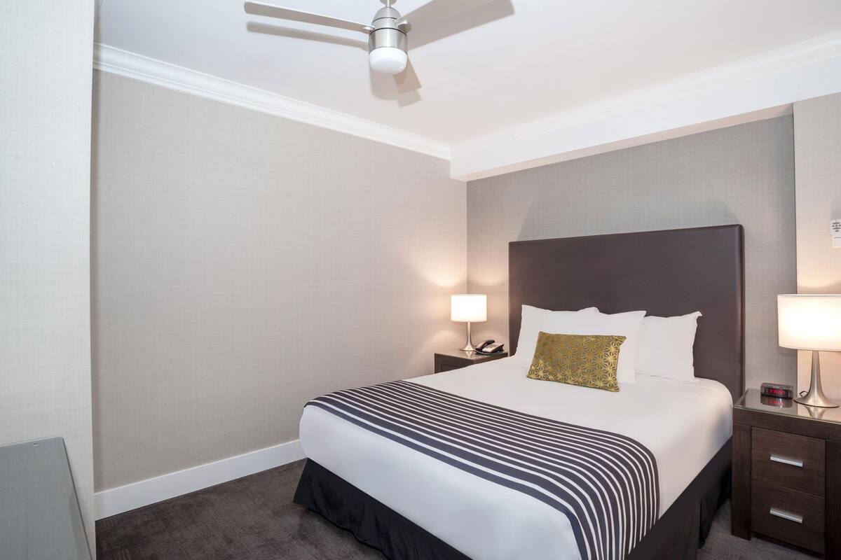 A hotel room with a bed, bedside tables, a ceiling fan, and a nightstand with a lamp.