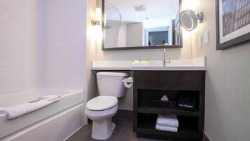A modern bathroom with a white bathtub, a white toilet, a vanity with a dark cabinet, and a large mirror above the sink.