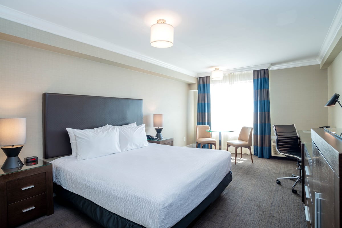 A hotel room with a large bed, a desk, a chair, and a lamp.
