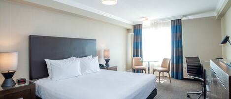 A hotel room with a large bed, a desk, a chair, and a lamp.