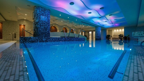 Een groot overdekt zwembad met een modern design, met een mozaïekwand en een plafond met een golfpatroon.