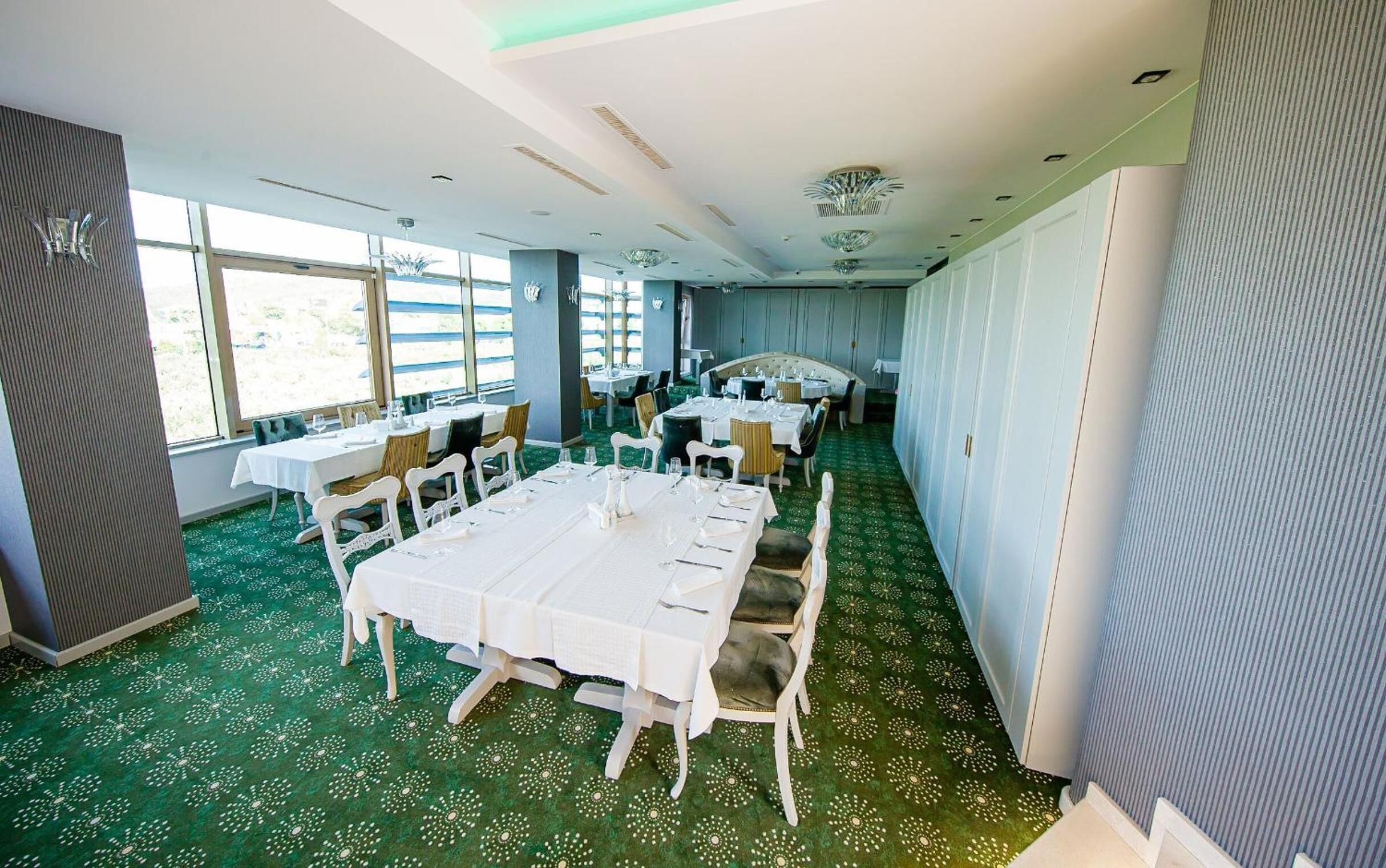 A dining area with tables set for service, large windows, and a green patterned carpet.