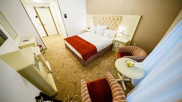 Quarto de hotel com uma cama grande, uma escrivaninha pequena, uma cadeira e uma janela.