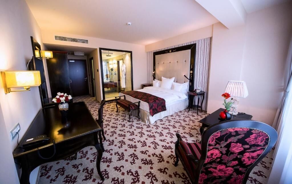 A hotel room with a bed, bedside tables, a desk, a chair, and a mirror.