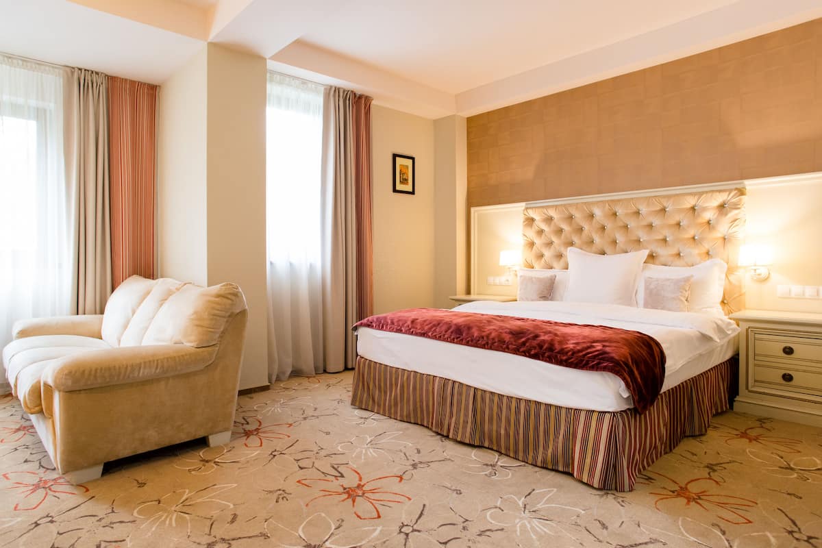 A hotel room with a large bed, a chair, and a nightstand with a lamp.