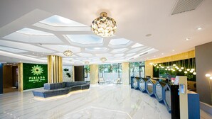 Een moderne hotellobby met een marmeren vloer, een receptiebalie, een zithoek en een grote kroonluchter.